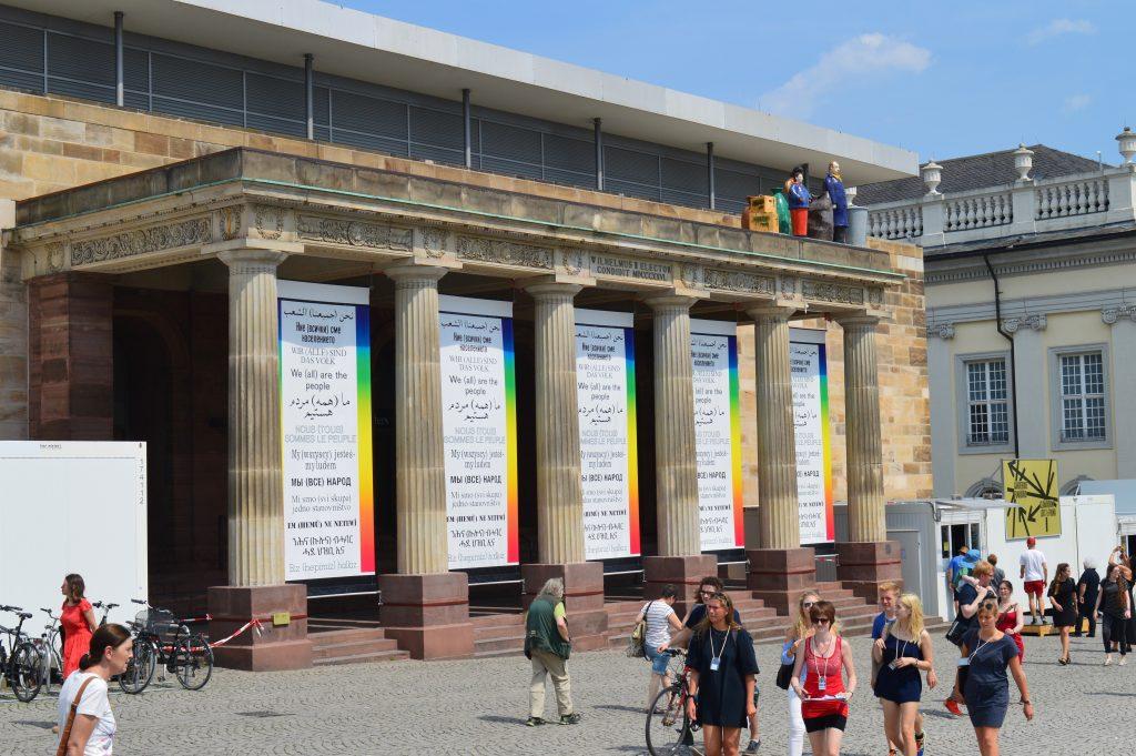 Hans Haacke, Wir (alle) sind das Volk—We (all) are the people, 2003/2017, cinq bannières, Friedrichsplatz, Cassel, © Hans Haacke/VG Bild-Kunst, Bonn 2017, documenta 14 / Thomas Schütte, Die Fremden, 1991/1992, céramique émaillée, documenta 9, photo : Mylène Palluel